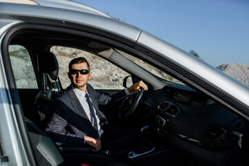Fototapeta na wymiar man businessman in a jacket, shirt, tie and sunglasses is driving a car.