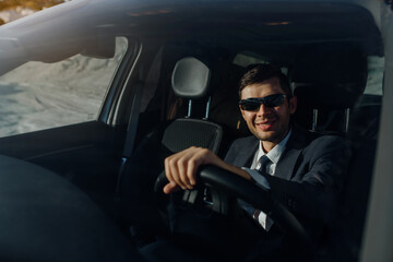 Fototapeta na wymiar man businessman in a jacket, shirt, tie and sunglasses is driving a car.
