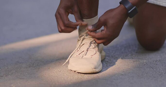 Unrecognizable african american sportsman fixing his sneakers during exercising, close up