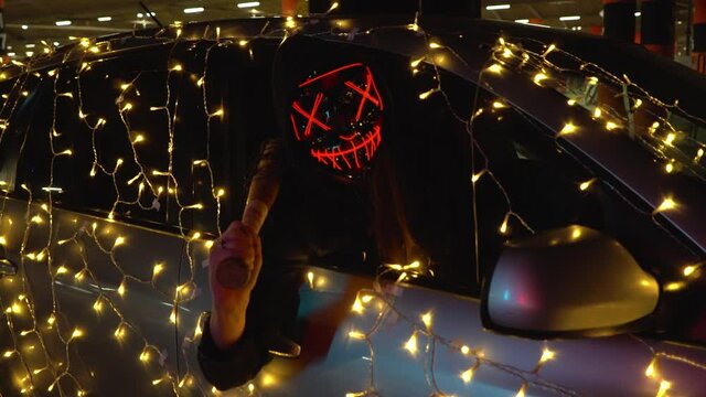 The killer in the scary mask is ready to clean up. A sweeper watches the victims from the car window with garlands.