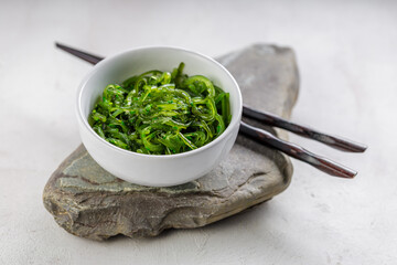 Croped photo of green wakame seaweed salad with chopstick at the restaurant
