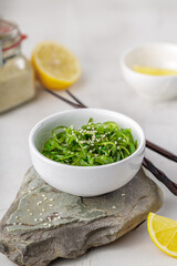 Croped photo of green wakame seaweed salad with chopstick and lemon at the restaurant