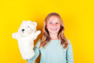 Cute little girl playing dolls theatre , holding fluffy white puppy in hand. Girl playing with...