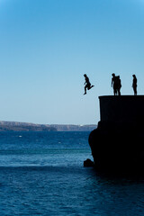 Group of friends jumping into mediterranean sea from rock cliff