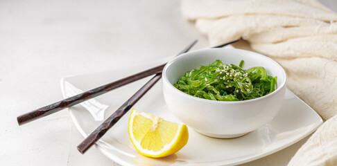 Croped photo of green wakame seaweed salad with chopstick and lemon at the restaurant