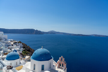 Fototapeta na wymiar Iconic view of Santorini, with typical blue dome church, sea and white facades. Detail of the roof of an orthodox church. Blue domed church along caldera edge in Oia, Santorini