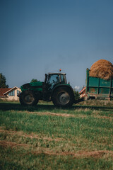 Farmer carries large round haystacks on his tractor.