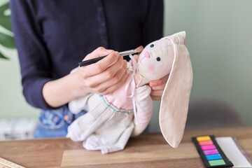 Young girl makes an author's handmade doll bunny, paints her cheeks with cosmetics