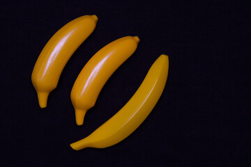 Three bananas on a dark background. Plastic toy