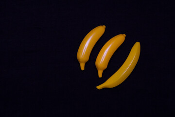 Three bananas on a dark background. Plastic toy
