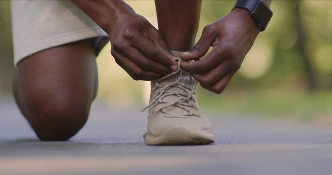 Closeup of black guy in sportswear tying his sneakers shoelaces before jogging outdoors