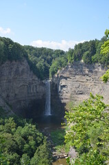 Breathtaking waterfall named Taughannock Falls that falls from a forest river over a huge rock face into a valley lake in sunny weather