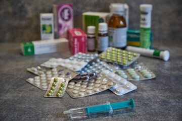 Closeup of a syringe and various pills in the background. Vaccine in a syringe. Collection of various pills and drugs.