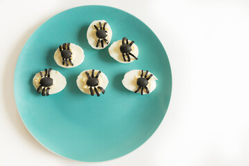 Appetizer for Halloween party: deviled eggs with black olives decorated as spider. On the blue plate and yellow table mat