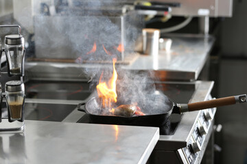 Cooking meat with burning flame in restaurant kitchen