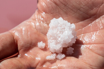 Hand holding pink white salt flake crystals formation near pink water surface. Spa resort sunny close-u