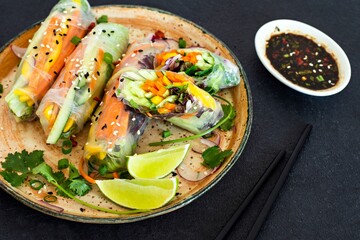 Fresh Asian appetizer Spring rolls (Nem) made from rice paper and raw vegetables and herbs with hot sauce on a dark background. Vietnamese Food