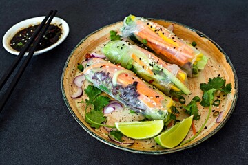 Fresh Asian appetizer Spring rolls (Nem) made from rice paper and raw vegetables and herbs with hot sauce on a dark background. Vietnamese Food