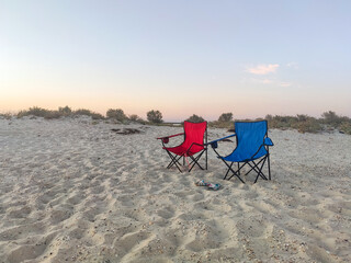 Couple of folding chairs on sandy beach in evening. Rest, camping.