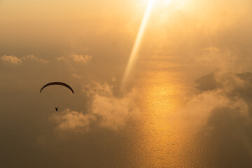 Silhouette of paraglider soaring over sea at sunset light