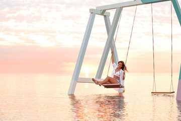 Young woman enjoying sunrise on swing over water