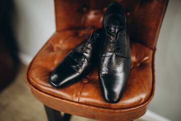 The groom is gathering in the morning. A gray chair. Men's Black classic patent leather shoes. A black bow tie. Wedding details