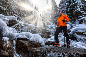Adventure man standing besides a beautiful waterfall in the winter wilderness. Sunrays. Taken in Joffre Lakes, North of Vancouver, British Columbia, Canada. Concept: Adventure, holiday