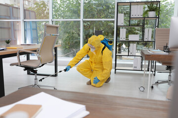 Janitor in protective suit disinfecting office to prevent spreading of COVID-19 - obrazy, fototapety, plakaty