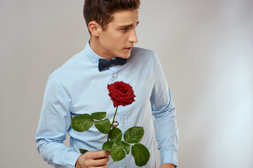 Handsome man with red rose blue shirt bow tie light background cropped view
