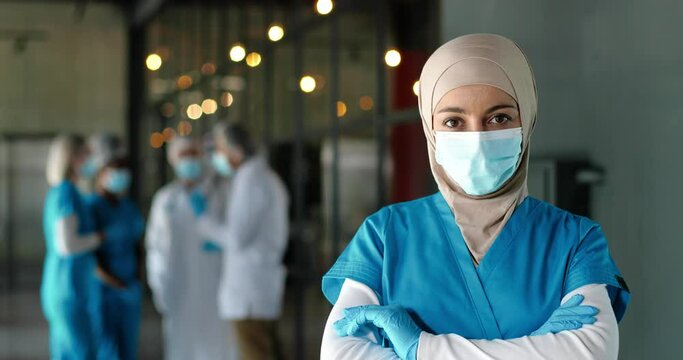 Portrait of Arab woman doctor in hijab, medical mask and gloves standing in hospital. Muslim female medic in traditional headscarf in clinic. Covid-19. Arabian nurse. Coronavirus. Protected.