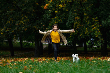 A cute little toddler girl giving a hug to her dog, a yellow in a park with autumn trees in the background