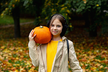 A little cute girl in an orange T-shirt makes an autumn application on paper, she glues autumn leaves, a child in the park on a mat, an autumn composition.
