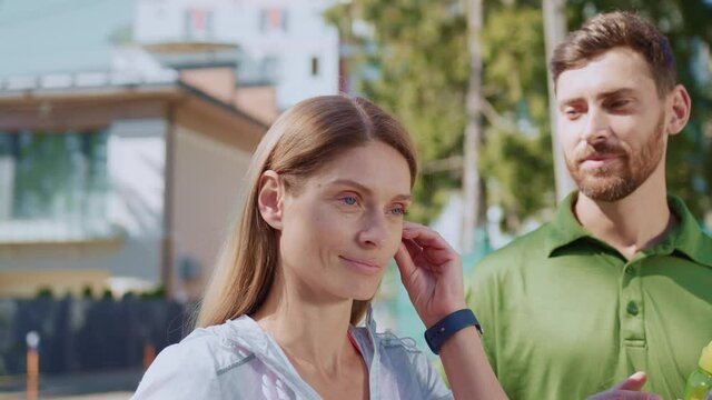Attractive caucasian woman athlete preparing for running wearing earphones to protect from boring man. Annoying bearded funny guy flirting to girl. Fun concept.