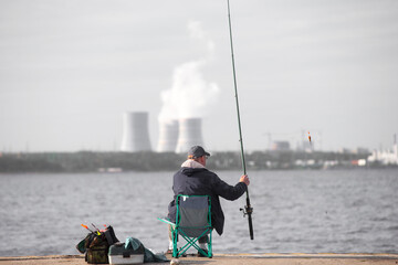 Fisherman on a concrete pier against the background of industrial structures