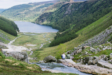 Fototapeta na wymiar a couple sitting at the top of Wicklow mountains with a view on a lake and the Glendalough Valley in Ireland