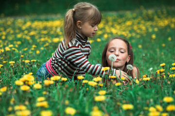 Cute five year old and eleven year old girls blowing dandelion seeds away in the meadow.