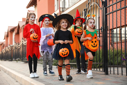 Cute little kids wearing Halloween costumes going trick-or-treating outdoors