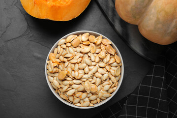 Raw seeds and fresh pumpkin on black slate table, flat lay