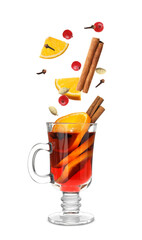 Cut orange, cranberries and different spices falling into glass cup of mulled wine on white background