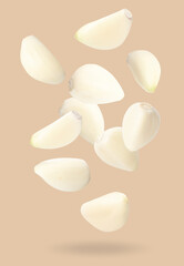 Many garlic cloves falling on beige background