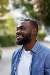 Close up portrait of a happy African American man. Handsome young man in blue denim shirt walking in the street and smiling.