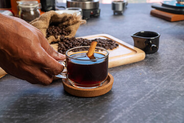 Hand of senior man holding glass cup of hot black coffee with coffee bean on wooden table in break time.