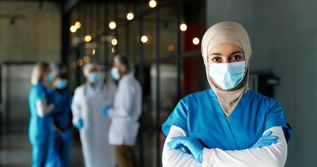 Portrait of Arab woman doctor in hijab, medical mask and gloves standing in hospital. Muslim female...