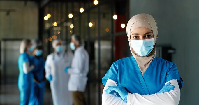 Portrait Of Arab Woman Doctor In Hijab, Medical Mask And Gloves Standing In Hospital. Muslim Female Medic In Traditional Headscarf In Clinic. Covid-19. Arabian Nurse. Coronavirus. Protected.