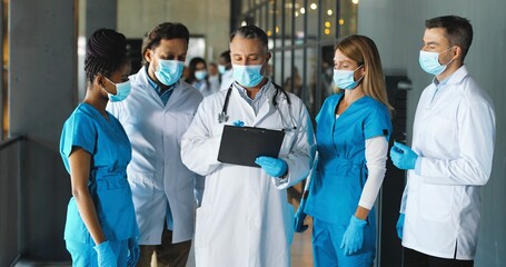 Head of clinic having consultation with workers doctors. Mixed-races males and females docs and nurses having conversation and looking at diagnosis. Coronavirus. Team of medics discussing covid-19.