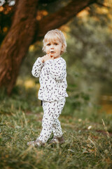 boy walking in a beautiful white suit against the background of nature, baby about one year old learning and playing outdoors.