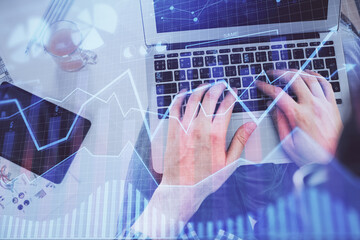 Double exposure of man's hands typing over laptop keyboard and forex chart hologram drawing. Top view. Financial markets concept.