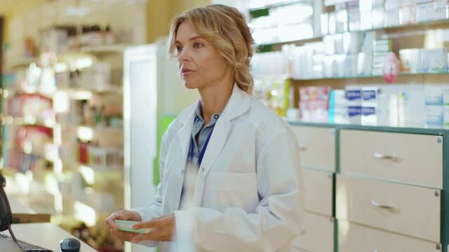 Serious tired woman pharmacist serving a customer in a drugstore. Conversation pharmaceutical client. Seller commercial health care buyer uniform. Slow motion