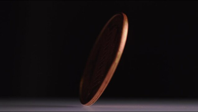 Super slow motion shot of pennies spinning around against a dark background
