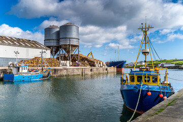 Small fishing boats in Wicklow commercial port with stacks of timber or wood logs being loaded on cargo ship in the background, Ireland © Dawid